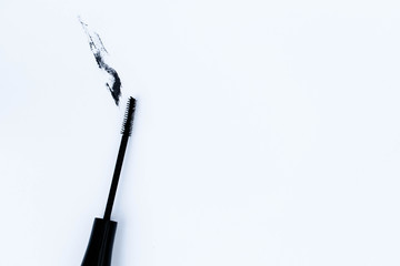 A mascara wand and mascara smudge of makeup against a plain white background with space for text