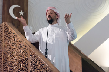 Wall Mural - Muslims young arabic Imam has a speech on friday afternoon prayer in mosque. Muslims have gathered for the friday afternoon prayer in mosque and are listening to the speech of imam