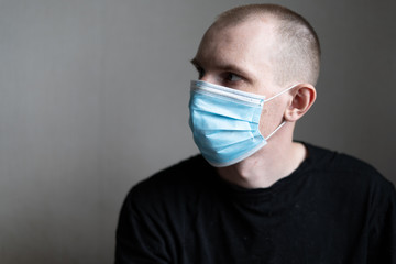 A guy in a medical mask and a black t-shirt is sitting on a light background