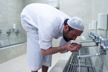 Wall Mural - Muslim man taking ablution for prayer. Islamic Religious Rite Ceremony Of Ablution. Young Muslim man perform ablution (wudhu) before prayer.