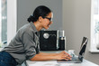 © Artem Varnitsin - Side view of a young woman working from her kitchen, typing on laptop