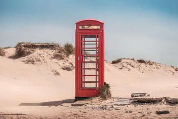 A vintage red telephone box in the sand dunes of a deserted beach near Sandbanks, Studland, Dorset, England, UK