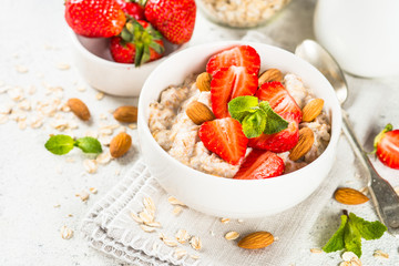 Wall Mural - Oatmeal porridge with fresh strawberry and nuts on white background.