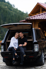 Wall Mural - Portrait of beautiful sexy blonde woman and man sitting in luxury dark car . Fashion and business concept. Idea for couple photoshoot with car. Valentines day, surprise.