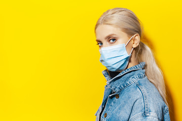 Wall Mural - Studio portrait of young blonde girl with blue eyes, wearing medical face mask against coronavirus. Background of yellow color.