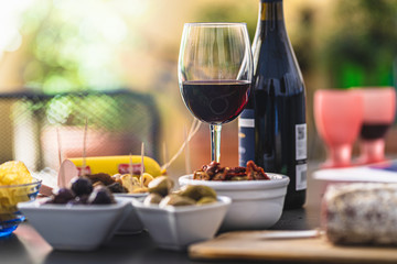 The courtyard table in the garden set with an assortment of Italian antipasti and a glass of red wine. People who spend the weekend at home during the lockdown for the coronavirus.