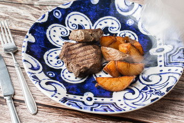 Grilled steak with baked golden potatoes on a wooden background. Top view. Delicious Recipe. Pork Fillet Cooked on Skillet for Dinner . Fried Juicy Meat Texture. Horizontal photo.