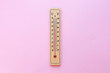 A classic wooden thermometer on pink background shows a high temperature of 20 degrees centigrade and 70 degrees fahrenheit