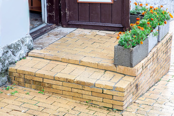 Wall Mural - brick threshold with a step at the open wooden entrance door with gray stone flowerpots for flowers, a closeup of architectural details.