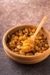 Wall Mural - Organic dried golden raisins in wooden bowl.Brown background, vertical format