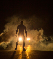 Mysterious figure in front of smoky car headlights