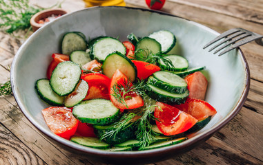 Wall Mural - Healthy vegetable salad of fresh tomato, cucumber, dill and spices and oil in bowl on rustic wooden background. Diet concept.