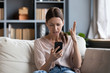 © fizkes - Confused angry woman having problem with phone, sitting on couch at home, unhappy young female looking at screen, dissatisfied by discharged or broken smartphone, reading bad news in message