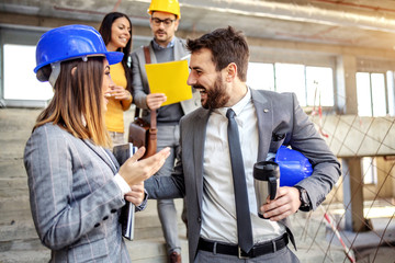 Wall Mural - Four dedicated architects standing in building in construction process and talking about important project. Man and woman in foreground chatting while other ones talking about ides.