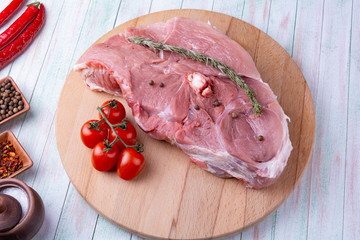 Wall Mural - piece of meat on a bone of rosemary, tomatoes, garlic and spices on a wooden round cutting board