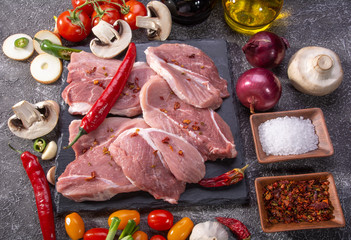 Wall Mural - Pork steaks, fresh vegetables, spices close-up on a textured background top view