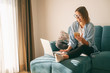 © olezzo - Young mature attractive woman sitting on a blue sofa in the living room at home with a smartphone in her hands in front of a laptop, online shopping