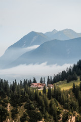 Wall Mural - Germany Bavaria Nature Alps Mountains. In the mountains against the sky, fog and green forest stands a house in the distance. Alpine houses, hotel. Summer. House among the mountain landscape