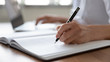 © fizkes - Female professional doctor hand making notes in medical journal using laptop computer sitting at desk. Woman physician, nurse or pharmacist wearing white coat writing in paper notebook. Close up view