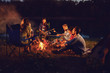 © Studio Romantic - A group of people sitting by the bonfire next to the tent at night in the summer in autumn.