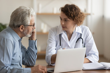 Wall Mural - Young female professional doctor physician consulting old male patient, talking to senior adult man client at medical checkup visit. Geriatric diseases treatment. Elderly medical health care concept