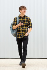 Full length happy young man walking with bag and cellphone by white background