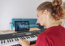 Young Girl Woman Learns To Play The Piano With A Teacher On A Video Conference From A Laptop. The Teacher On The Screen Explains On The Internet. Education Video Calls Self Education
