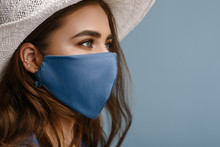 Woman Wearing Stylish Protective Face Mask, Posing On Blue Background. Trendy Fashion Accessory During Quarantine Of Coronavirus Pandemic. Close Up Studio Portrait. Copy, Empty Space For Text