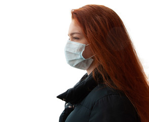 Horizontal shot of ill redhead girl wears medical mask to protect from catching disease, looking into the distance, in black jacket, stands outdoor, suffers from epidemic illness, isolated background