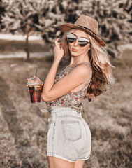 Stylish woman in hat walks on the beach at sunset.