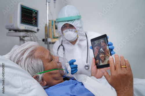 Doctors and nurses are helping elderly corona virus/covid-19 infected patients in the ICU/ hospital, communicating to his family using tablet video call.