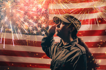 Memorial day. A female soldier in uniform salutes against the background of the American flag with fireworks. Side view. The concept of the American national holidays and patriotism