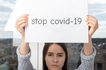 Wall Mural - Girl holding a sheet with the words stop covid-19