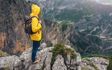 Middle Age Man Traveler In Raincoat And Backpack Enjoying View Of Mountains.