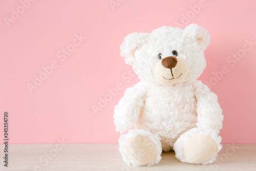 Cuadros en Lienzo Smiling white teddy bear sitting on table at pastel pink wall background