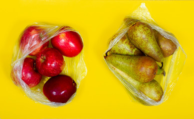 Ecology concept: fruits (red apples and green pears) in two plastic bags on yellow backround. Top veiw.