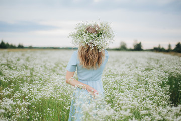 beautiful blonde girl in a field of daisies. wreath of wildflowers on his head. woman in a blue dress in a field of white flowers. charming girl with a bouquet of daisies. summer tender photo