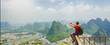 Hiker with backpack take a picture on his smartphone from top of the hill with view on Yangshuo city with mountains around. China. Banner edition.