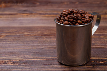 Steel mug overfilled with cup. Brown wooden table surface.