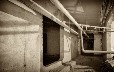 A multi-storey residential building made of reinforced concrete in the city. Basement. Earthen floor, wiring pipes with water and hot heating of apartments. Black and white image. Sepia.