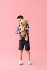 Cute little boy with toy bear on color background