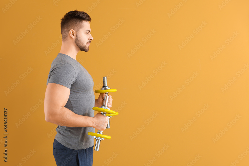 Sporty young man training with dumbbells on color background