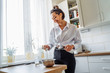 © Daria - DIY home cooking concept. A bright brunette woman sifting the flour for pancakes through a sieve, salting the dough, adding milk. Young woman smiling, loves to cook in a beautiful modern kitchen.