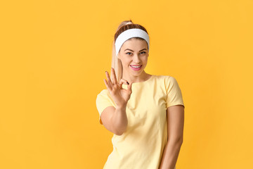 Portrait of beautiful young woman showing OK gesture on color background