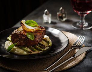 Beef steak with mashed potatoes and asparagus on a black plate. Dinner at the restaurant