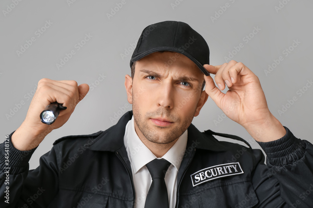 Male security guard with flashlight on grey background