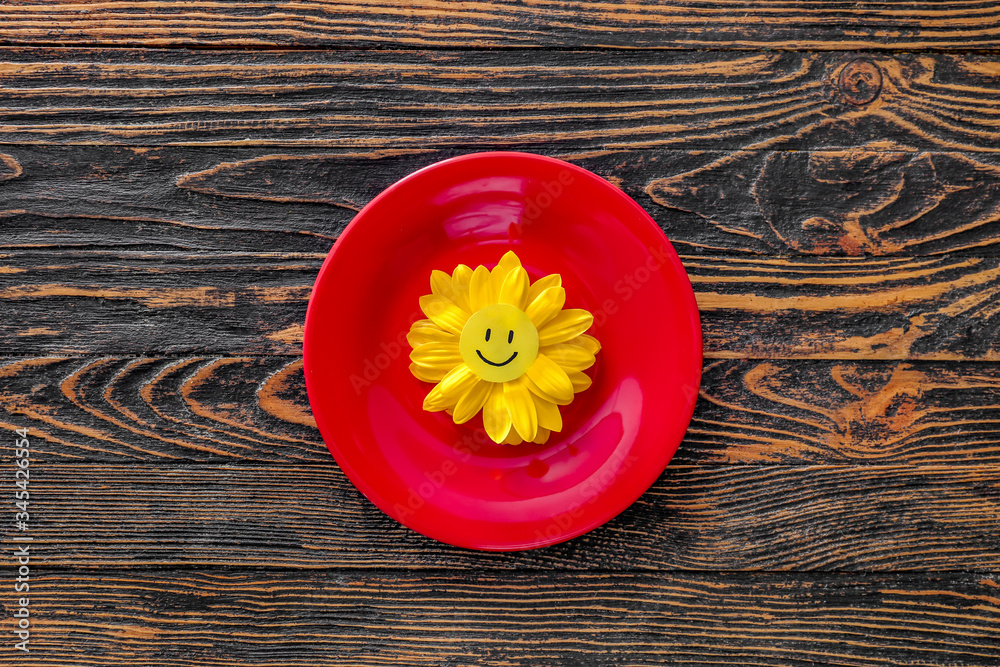 Plate with flower and paper smile on wooden background