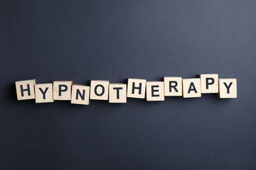 Wooden blocks with word HYPNOTHERAPY on black background, flat lay