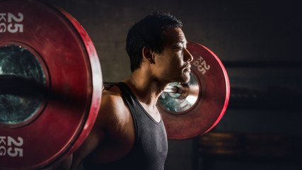 asian strong athletic man having workout and bodybuilding with barbells weight lifting backsquat style in gym and fitness center in dark tone