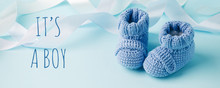It's A Boy Text. Blue Baby Knitted Shoes For Newborns On Blue Background, Minimal Baby Shower, Newborn Party Background, Copy Space